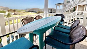 A balcony with a table and chairs, overlooking a building and a view of the beach. - OW 3201-Flirty Flamingo: Oceanview condo in Oak Island, sleeps 10, pet-friendly. (Oak Island)