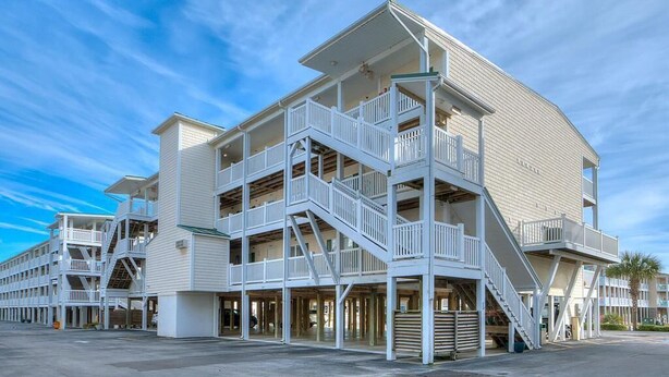 A multi-story hotel with outdoor balconies and a central staircase. - OW 3201-Flirty Flamingo: Oceanview condo in Oak Island, sleeps 10, pet-friendly. (Oak Island)