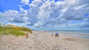 A beach with sand, a dune, and a cloudy sky. - OW 3201-Flirty Flamingo: Oceanview condo in Oak Island, sleeps 10, pet-friendly. (Oak Island)