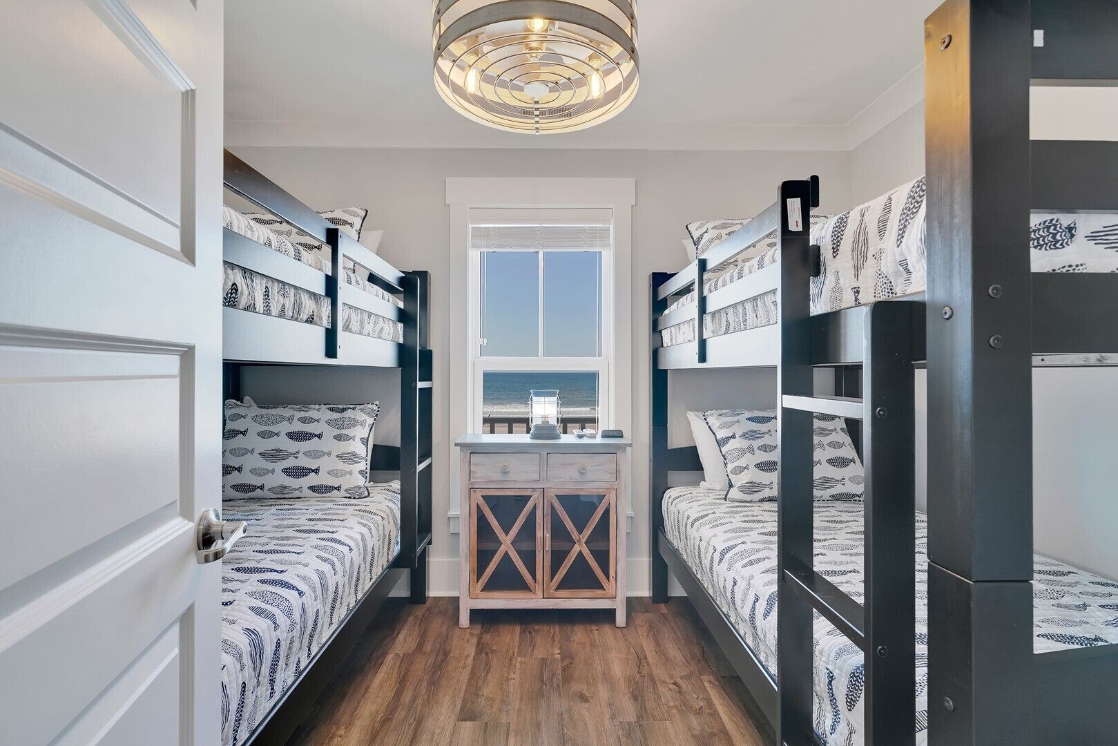 Une chambre avec des lits superposés, une armoire en bois, une fenêtre donnant sur un beau paysage et un luminaire au plafond.