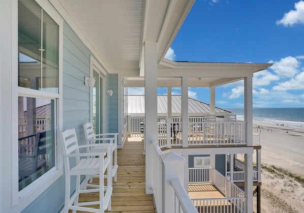 A covered porch with white railings, a wooden deck, and a view of the beach.