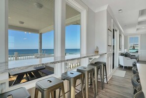 A modern kitchen with a large window overlooking the ocean, bar stools, and a seating area with a view.