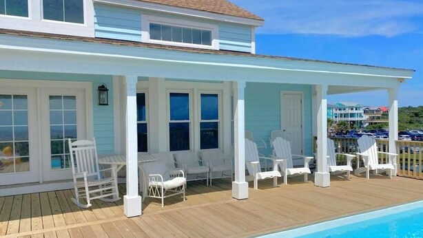 Ein zweistöckiges Haus mit überdachter Terrasse und Schwimmbecken.