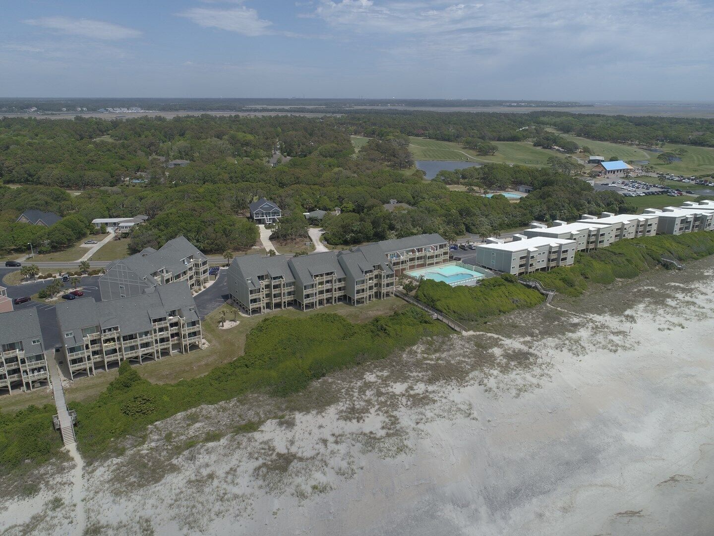 A coastal hotel with multiple buildings, a swimming pool, and a beach area.
