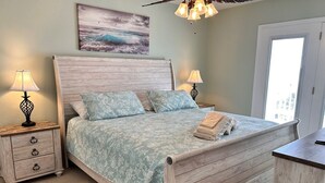 A bedroom with a wooden bed, two bedside lamps, a nightstand, a window, and a painting on the wall.