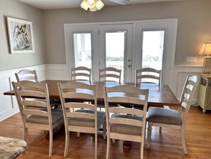 A dining area with a wooden table and six chairs, a ceiling fan, and a door with windows. - Experience beachfront bliss at Serendipity, Oak Island's spacious 5BR retreat. (Oak Island)