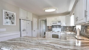 A kitchen with white cabinets, a granite countertop, a built-in oven, and a backsplash with a stone pattern.