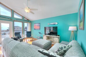 Ein geräumiges Wohnzimmer mit großem Fenster, Deckenventilator, Fernseher und einer Wand in Türkis.