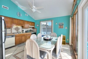 A kitchen with wooden cabinets, a white refrigerator, a glass dining table with wicker chairs, and a ceiling fan.