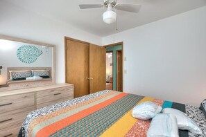 A bedroom with a bed, a dresser, a ceiling fan, and a door leading to another room.