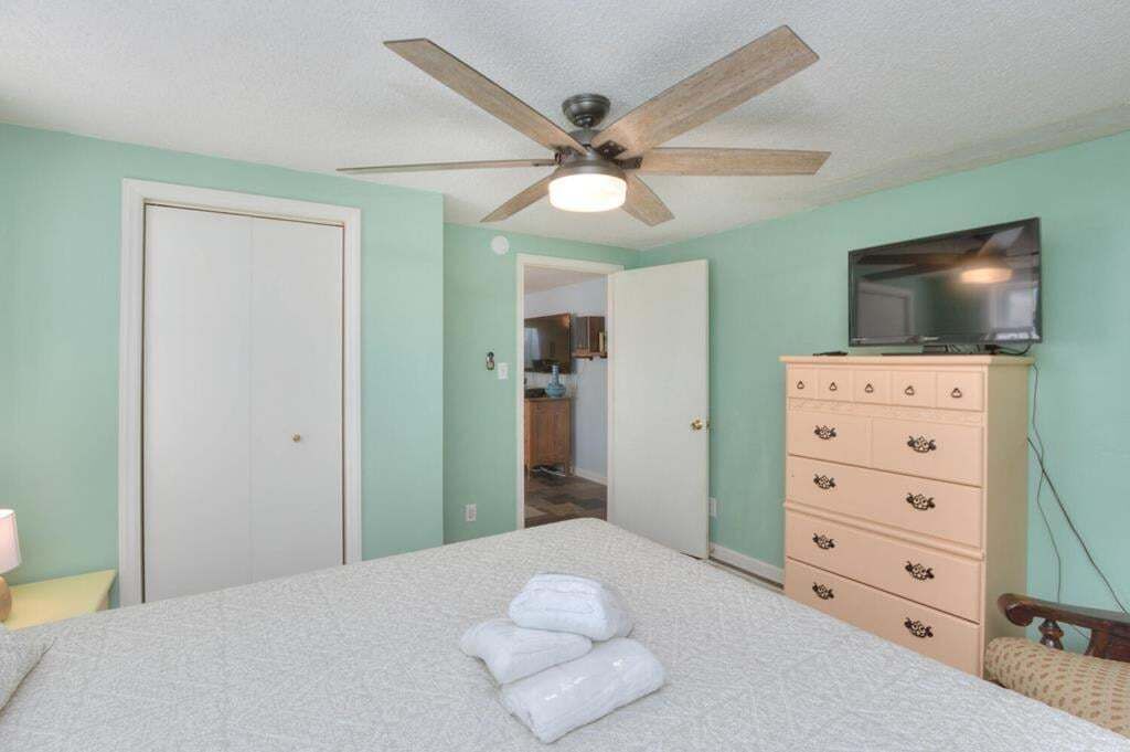 Ein Schlafzimmer mit Bett, Deckenventilator, Kommode und Fernseher.