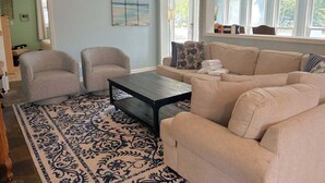 Ein Wohnzimmer mit einem beigefarbenen Sofa, zwei Sesseln, einem Couchtisch und einem gemusterten Teppich.