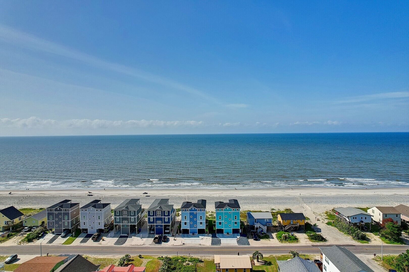 A beachfront property with a row of blue and gray houses, a sandy beach, and the ocean in the background.
