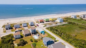 An aerial view of a coastal residential area with houses, a beach, and a pier in the distance. - Stay at Rangers Rendezvous, a charming 3-bedroom home in Oak Island with ocean views. (Oak Island)