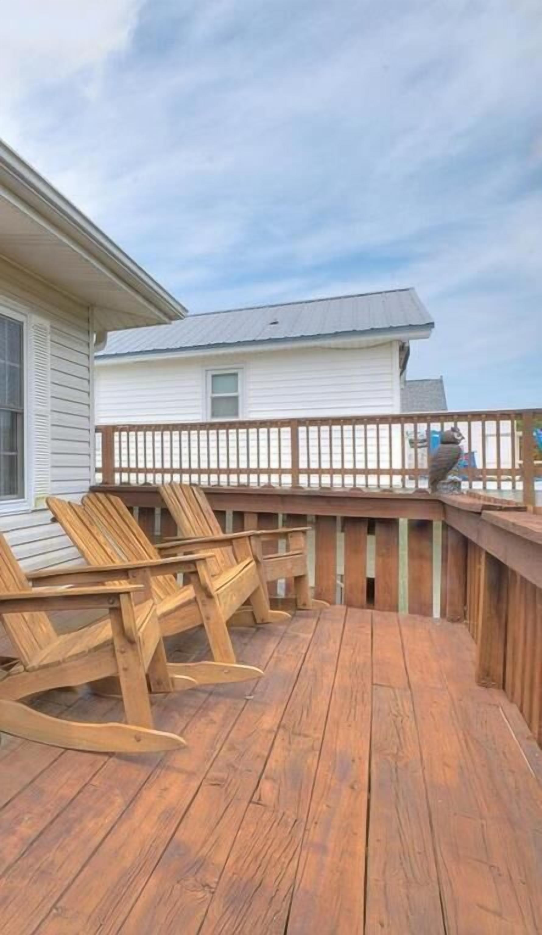 A wooden deck with Adirondack chairs and a railing, overlooking a residential area.