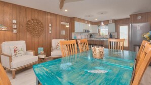 Uma sala de jantar com uma mesa azul-turquesa, cadeiras de madeira e um ventilador de teto.