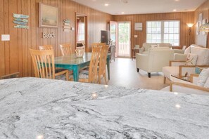 A spacious living area with a marble dining table, wooden chairs, a sofa, and a television.