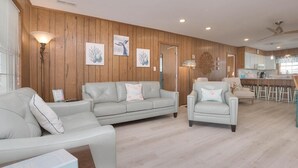 Uma sala de estar moderna com parede revestida de madeira, um sofá, uma poltrona e uma área de jantar com banquetas.