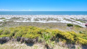 Una playa con vista despejada del océano, dunas de arena y vegetación escasa.