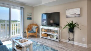 Un salon avec une grande télévision, un fauteuil en osier, une table basse et une plante.