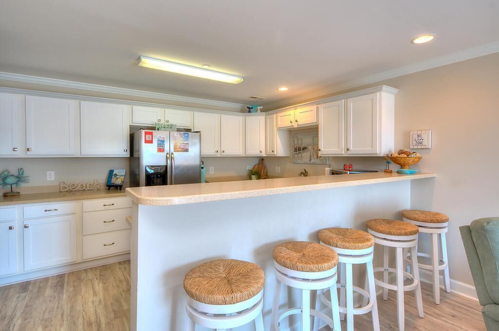 A modern kitchen with white cabinets, a stainless steel refrigerator, and a bar area with stools.