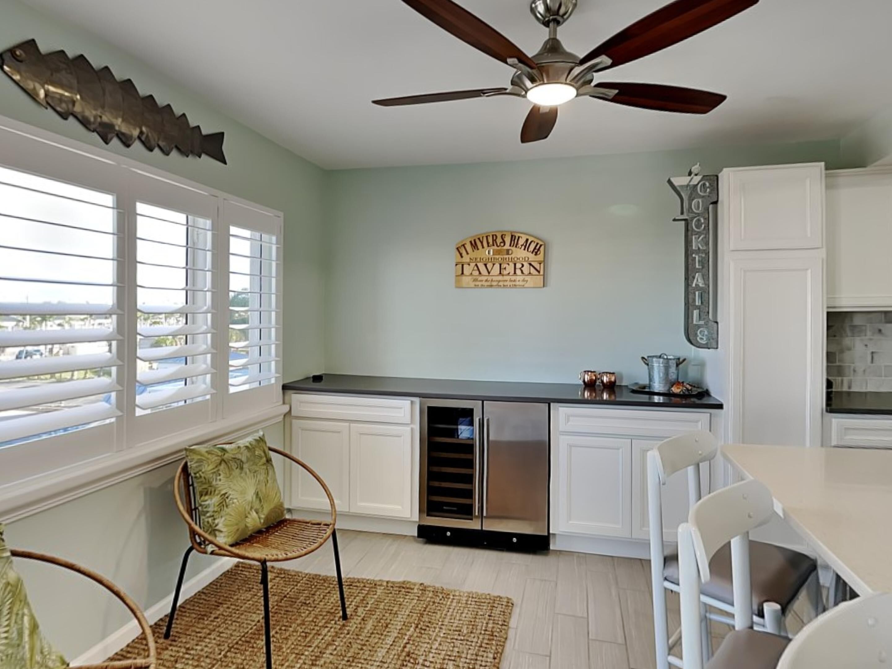 A kitchen with white cabinets, a stainless steel dishwasher, a ceiling fan, and a window with blinds.