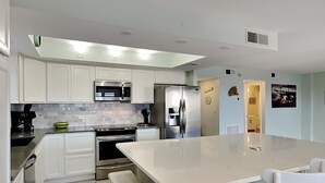 A modern kitchen with white cabinetry, stainless steel appliances, and a large island with bar stools. - Sand Caper by Distinctive Beach Rentals (Fort Myers Beach)