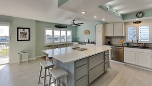 A spacious kitchen with a large island, white cabinetry, and a view of the outdoors. - Sand Caper by Distinctive Beach Rentals (Fort Myers Beach)