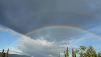 A natural landscape with a rainbow arching over a forested area and a mountain in the background.