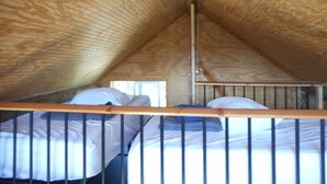 Une chambre de type dortoir, avec des lits superposés, des poutres en bois et une fenêtre.