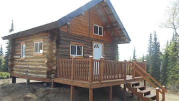 Une cabane en rondins dotée d’une terrasse en bois et d’un escalier menant à une porte.