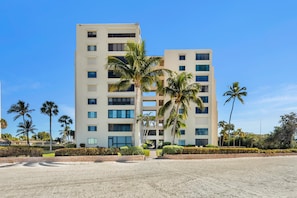A multi-story hotel with a modern design, featuring a central courtyard with palm trees and a sandy ground area.
