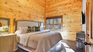 A wooden cabin bedroom with a bed, a nightstand, a window, and a door. - Toccoa Sunnyside ~ Minutes to Downtown Blue Ridge ~ Hot Tub! (Blue Ridge)