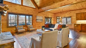 A spacious log cabin with a high ceiling, large windows, a fireplace, and a cozy seating area. - Toccoa Sunnyside ~ Minutes to Downtown Blue Ridge ~ Hot Tub! (Blue Ridge)
