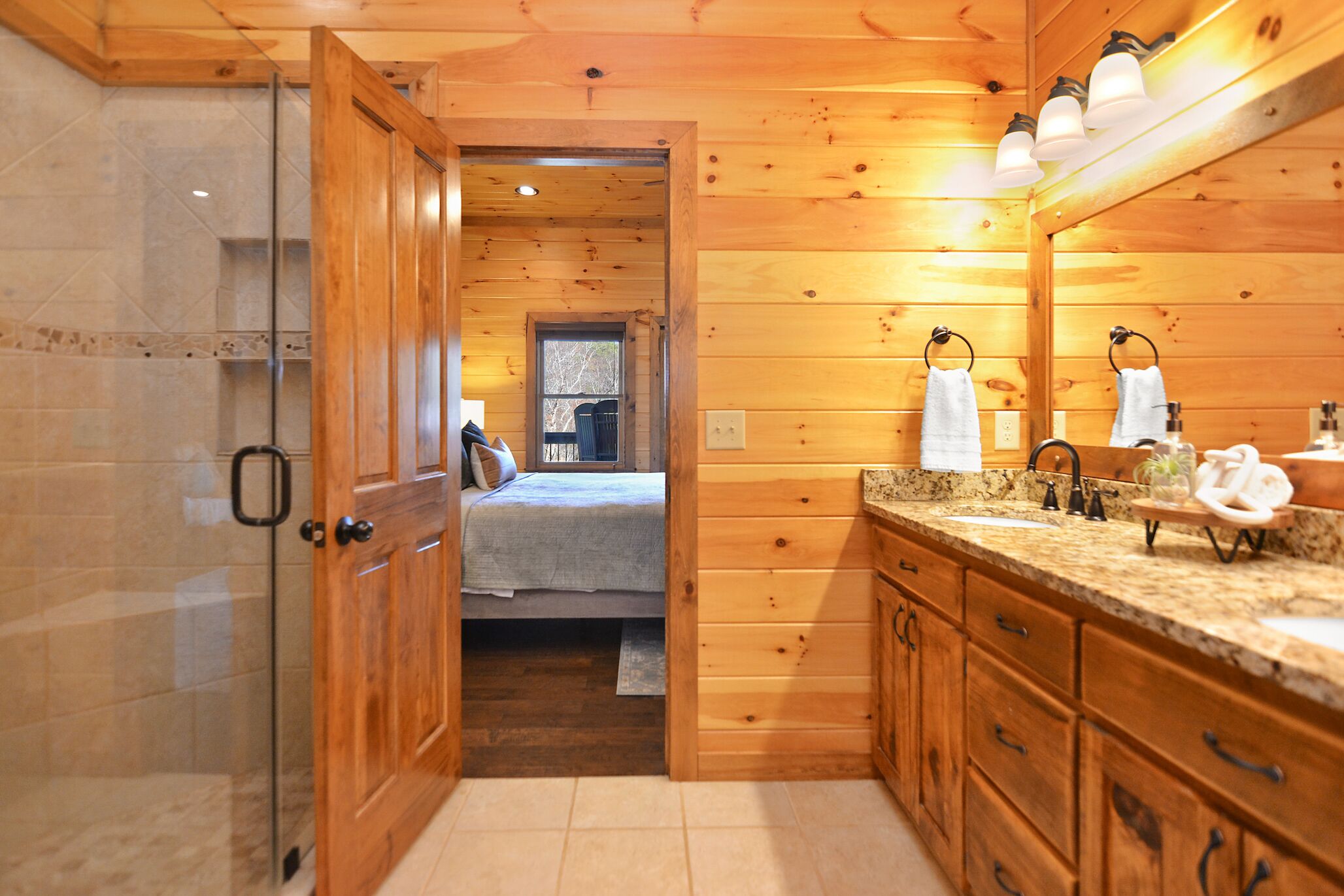 Un baño estilo cabaña de madera con ducha, lavamanos con encimera de granito y espejo sobre el lavamanos.