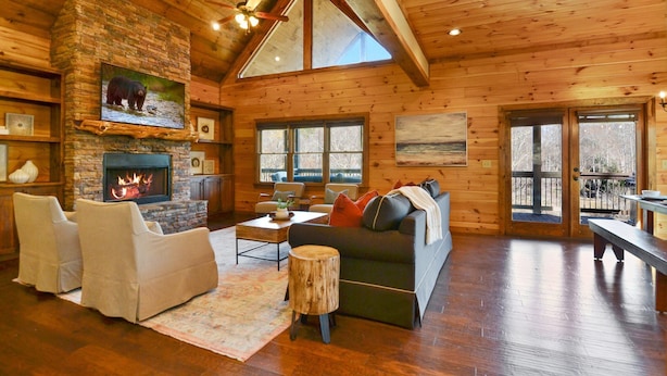 A log cabin interior with a fireplace, wooden furniture, and large windows. - Toccoa Sunnyside ~ Minutes to Downtown Blue Ridge ~ Hot Tub! (Blue Ridge)