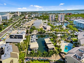 An aerial view of a marina with boats docked, surrounded by buildings and a beach in the background. - Santa Maria by Distinctive Beach Rentals (Fort Myers Beach)