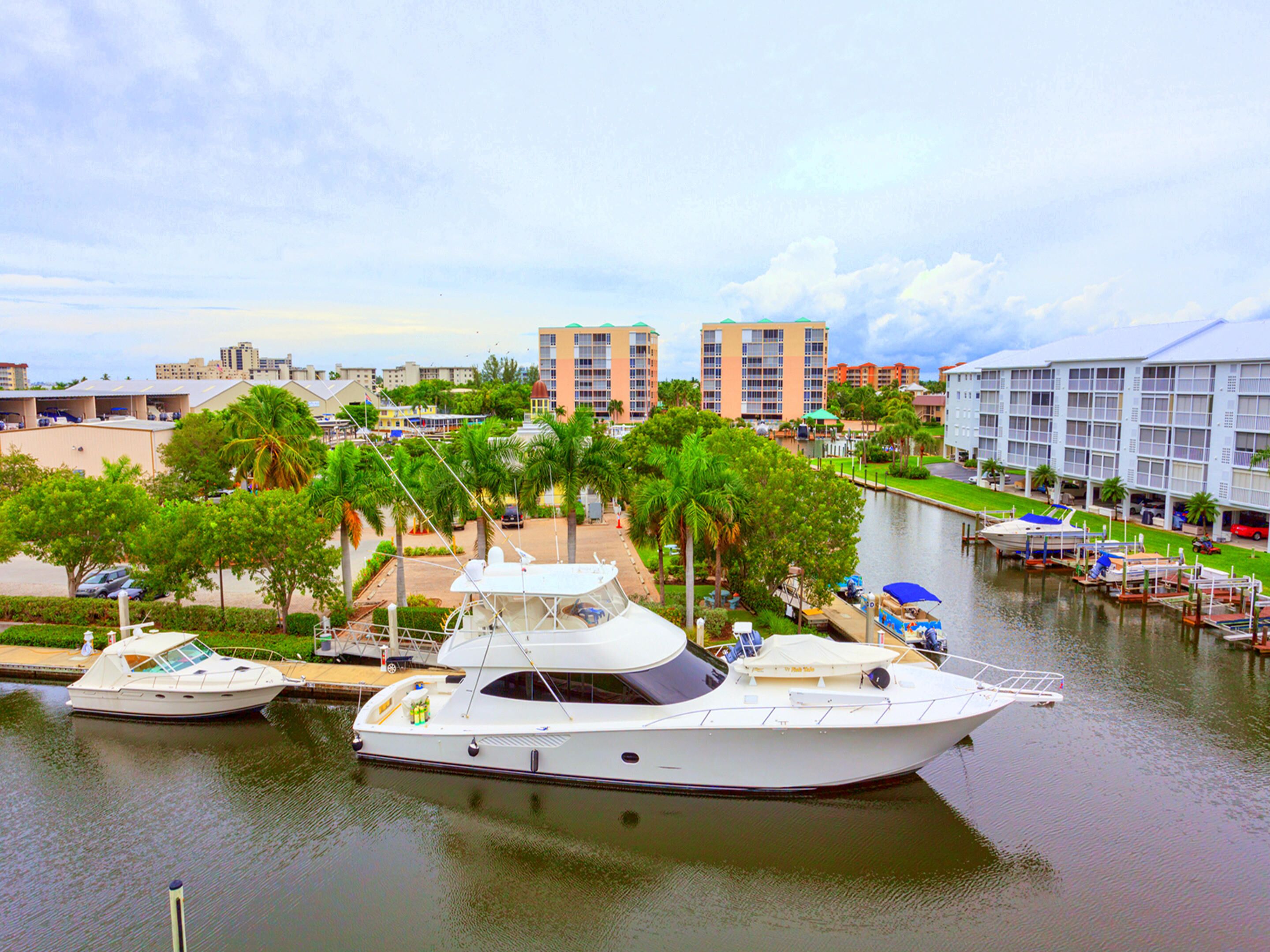 A marina with several boats docked, surrounded by palm trees and buildings.
