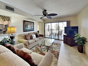 A living room with a sofa, a coffee table, a television, and a balcony with outdoor furniture. - Santa Maria by Distinctive Beach Rentals (Fort Myers Beach)