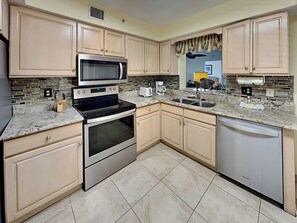 A modern kitchen with light wood cabinets, stainless steel appliances, a granite countertop, and a tiled floor. - Santa Maria by Distinctive Beach Rentals (Fort Myers Beach)