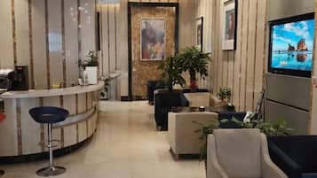 Een hotel lobby met een receptiebalie, een zithoek en een aan de muur bevestigde televisie.