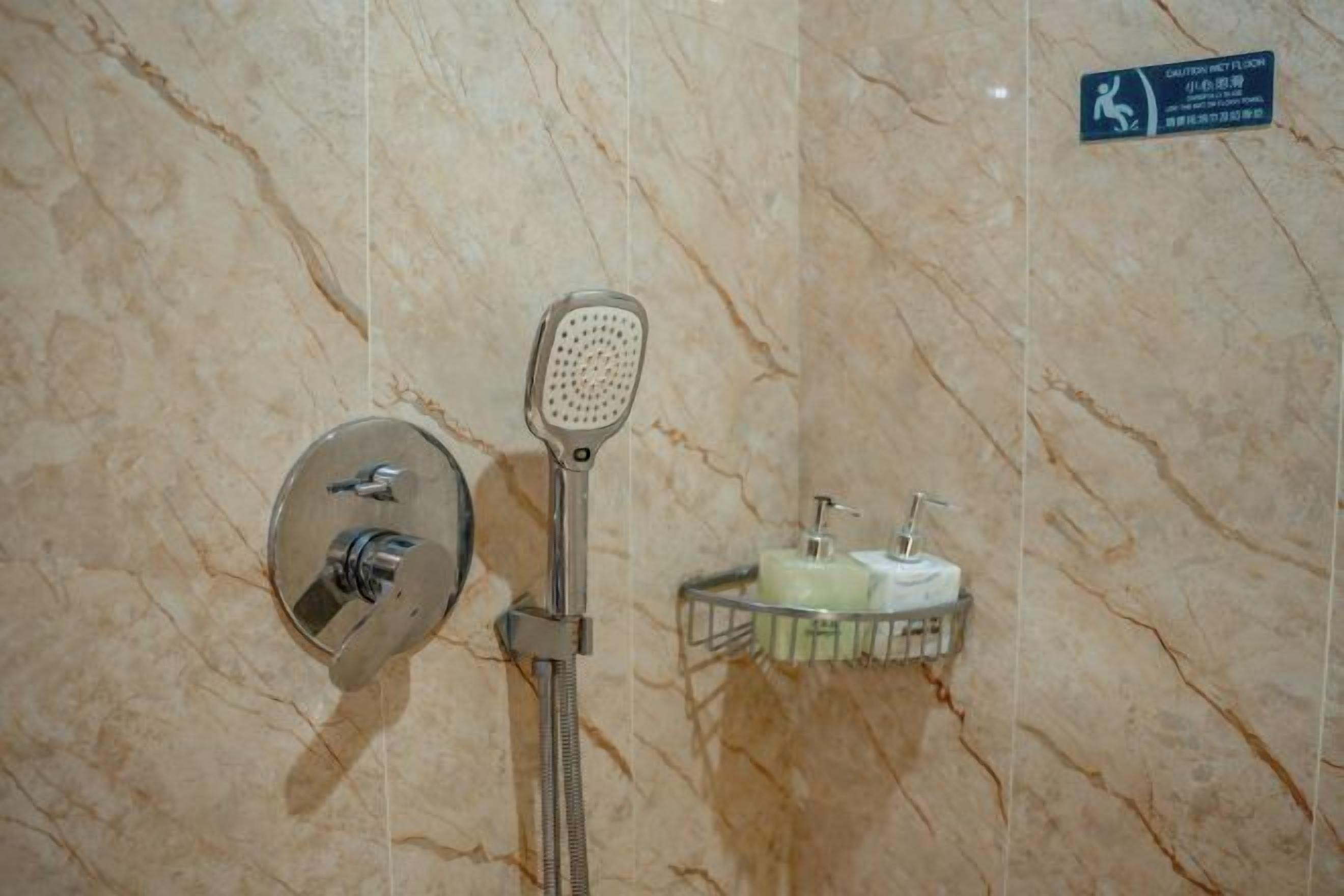 A bathroom with a shower, a hand dryer, and a soap dispenser on a marble wall.
