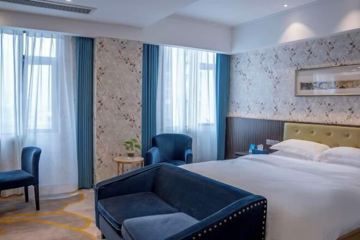 A hotel room with a bed, two armchairs, a small table, and a window with curtains.