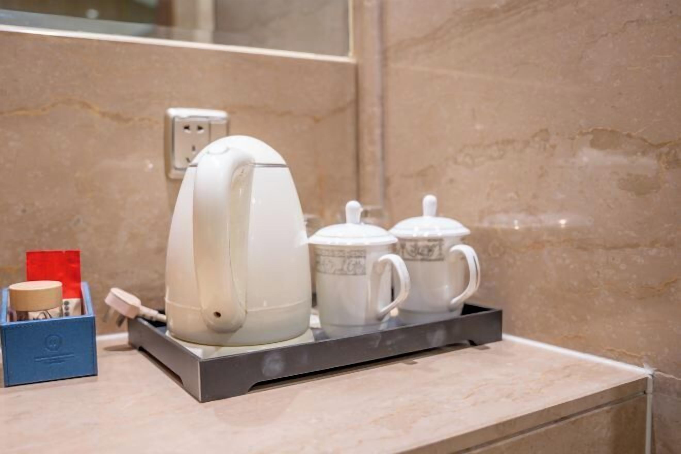 Uma cafeteira, duas chávenas e uma caixa com um objeto vermelho numa bancada.