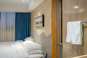 A hotel room with a bed, a wooden panel wall, a framed picture, and a towel rack.
