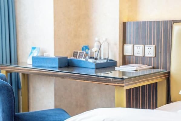 A hotel room with a bed, a desk with a laptop, a chair, and a small table with toiletries.