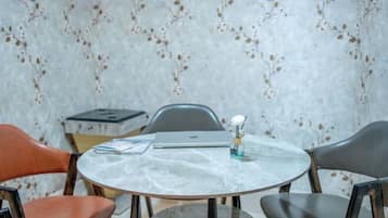 Una mesa redonda con cubierta de mármol, rodeada por cuatro sillas, una de ellas naranja. Sobre la mesa hay un ordenador portátil y un pequeño florero con una flor.