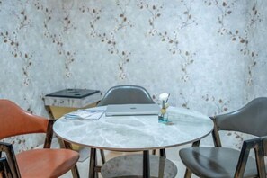 Ein runder Tisch mit Marmorplatte, umgeben von vier Stühlen, einer davon ist orange. Auf dem Tisch stehen ein Laptop und eine kleine Vase mit einer Blume.