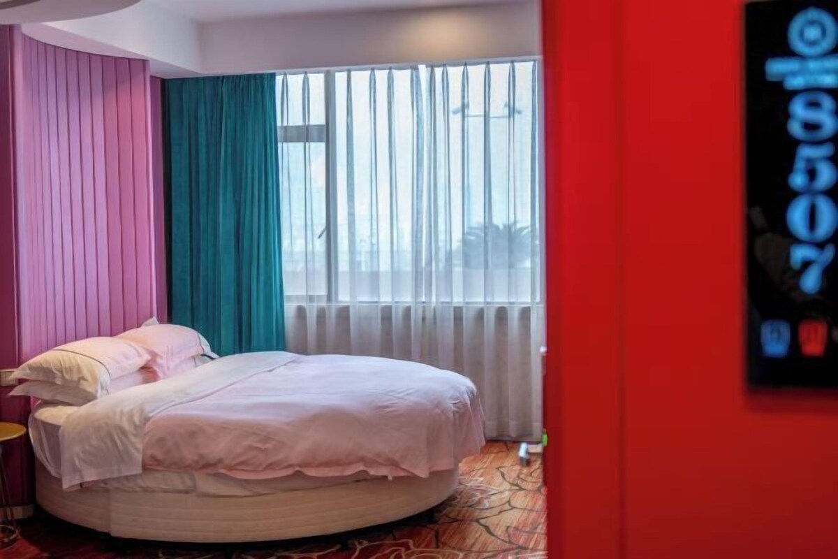 A hotel room with a bed, a window with curtains, and a wall-mounted phone.