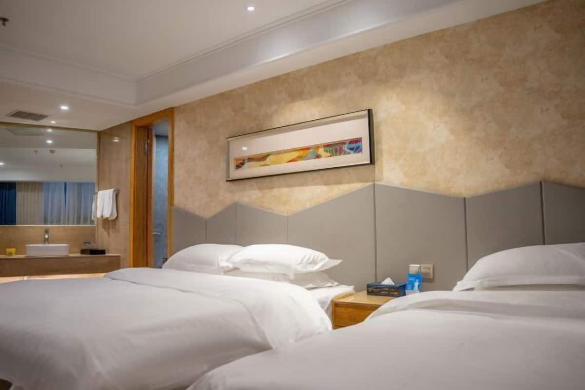 A hotel room with two beds, a large painting on the wall, a bathroom with a sink, and a mirror.